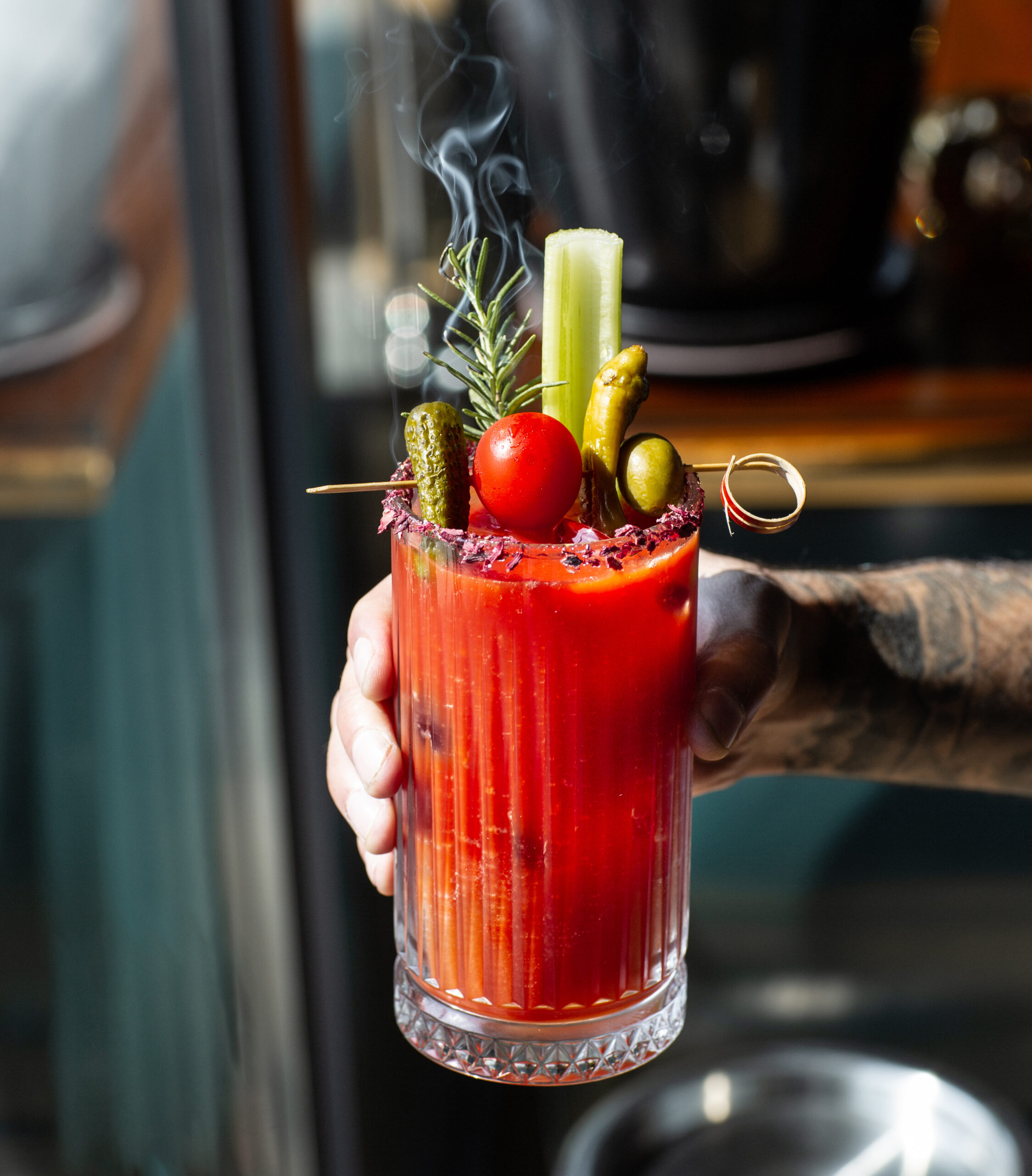 man holding tomato juice garnished with celery stick olive pickled cucumber pepper